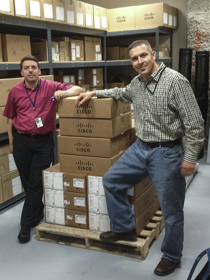 Two men standing by a pallet of boxes.