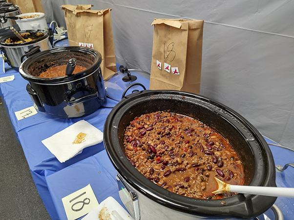 Karen Saylor’s entry (#18, foreground) and Jim Farling’s third-place entry (#17, background, left) were both among the spiciest. The competition coordinators placed a “spiciness scale” of chili stickers on each entry’s voting bag so attendees knew what to expect. (Photo by Samuel Lopez.)