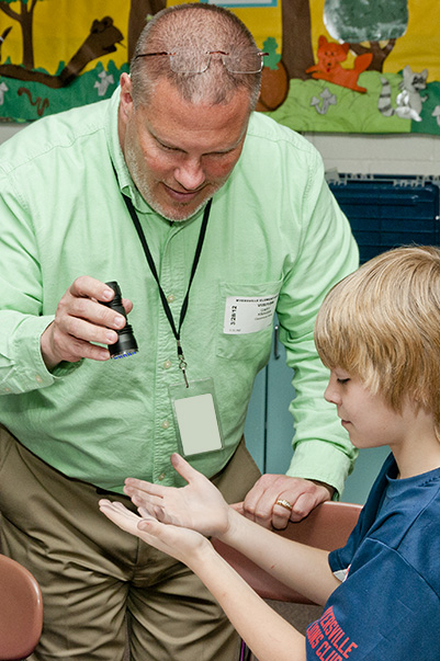 Gary Krauss, senior subcontracts administrator, Contracts and Acquisitions Directorate, works with a student during a “crime scene investigation” Elementary Outreach Program activity. (Photo by Richard Frederickson, staff photographer)