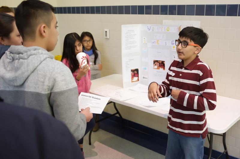 A science club member presents his group’s research to a guest.