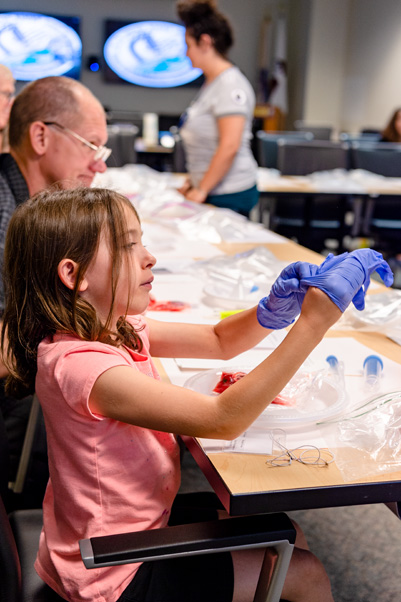 A child dons safety gloves and prepares to extract DNA from a strawberry at the “Spool Strawberry or Banana DNA” program, sponsored by the U.S. Army Center for Environmental Health Research.