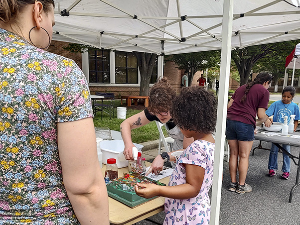 Kylee Stenersen (center), another staff member at the EHS booth, teaches a child about runoff in an activity using sprinkles and water to simulate pollution and rainfall, respectively.