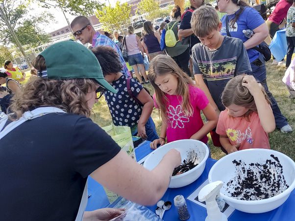 One of the many hands-on activities in the hub area: Kylee Stenersen helps children make wildflower seed balls to take home and plant.