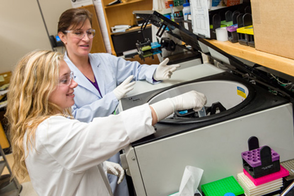 Werner H. Kirsten intern Nicole Pohida loads a centrifuge under the instruction of Kim Klarmann, Ph.D., Hematopoiesis and Stem Cell Biology Section.