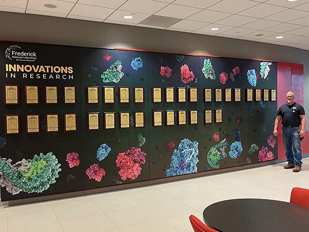 The patent plaque wall was installed by Keith Zecher (right), of the Facilities Maintenance and Engineering Directorate, who was instrumental in creating the display. (Photo credit: Paul Horning)