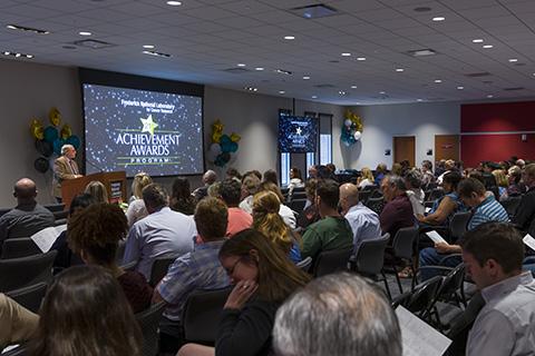 A crowd of people watches Dr. Dmitrovsky speak at a past achievement awards ceremony