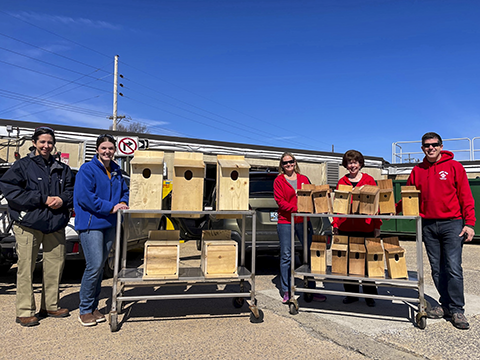 Five people pose alongside two wheeled carts laden with wooden birdhouses