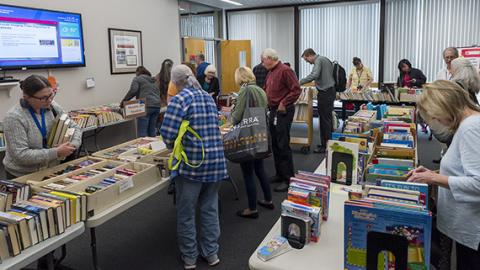 Photo: a small crowd of visitors peruses rows of tables lined with books at the Book and Media Swap