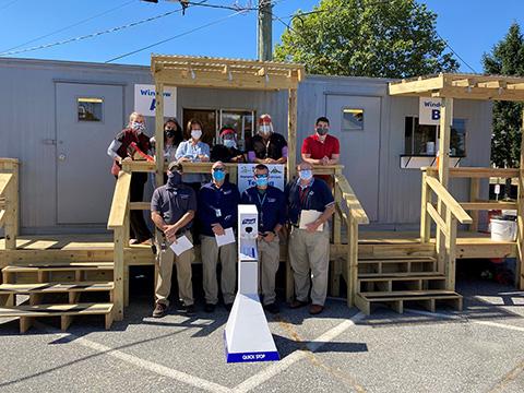 A group of people wearing surgical masks standing in front of the new COVID testing clinic, a trailer