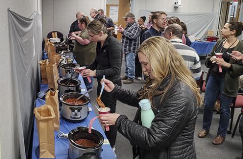 A crowd of people lined up at pots of chili
