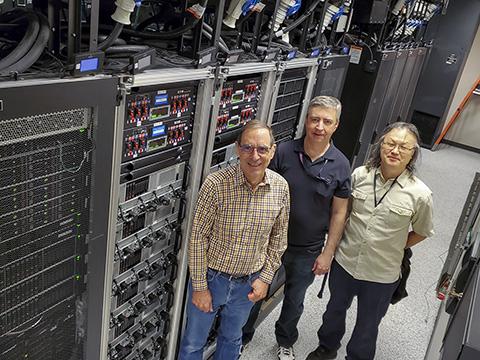 Three men standing in front of a row of servers