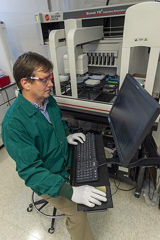 Todd Hartley working at a computer, with the Biomek in the background behind him