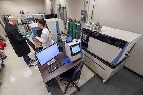 Photo of Ben Orsburn and coworker Carly Van Wagoner flanked by the Fusion and two other mass spectrometers