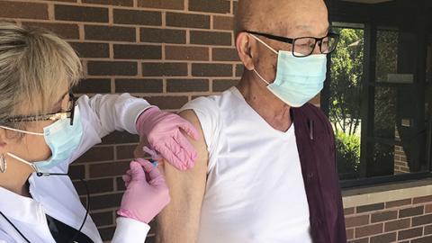 Photo of a nurse administering a vaccine to a man outside