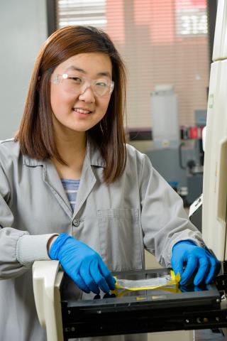 Photo of Allison Kang smiling while working with a scientific instrument in the laboratory