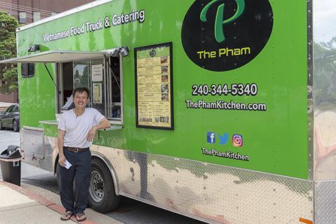 Photo of An Pham, owner of The Pham, standing in front of his bright green food truck