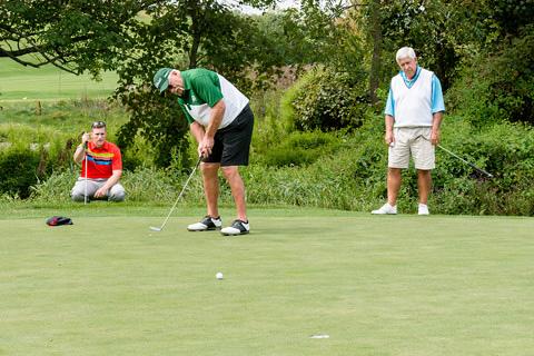 Man putts as two players watch