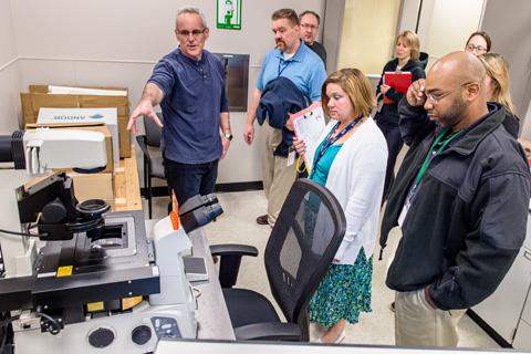 Group of people gathered around laboratory equipment.