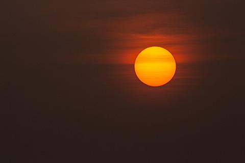 The sun, colored orange and covered by clouds