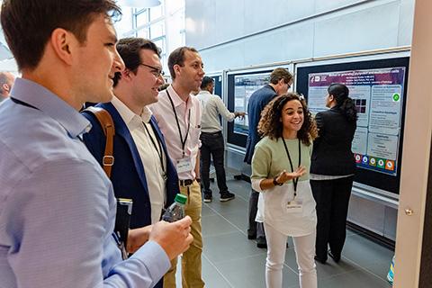 A group of business professionals gather around a research poster