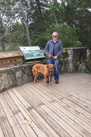 Photo of Dr. Ethan Dmitrovsky posing with his dog, Shep, on a wood-and-stone bridge during a walk