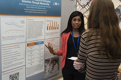 Photo of intern Ishika Srivastava standing at her poster and explaining her project to another student
