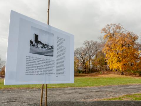 One of the signs detailing the history of Fort Detrick, with a yellow tree in the background.