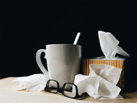 a table with a mug, tissue box, crumpled tissues, and glasses