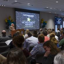 A crowd of people watches Dr. Dmitrovsky speak at a past achievement awards ceremony