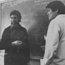 Black-and-white photograph of two scientists at a chalkboard