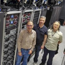 Three men standing in front of a row of servers