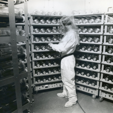 A scientist in a protective suit surrounded by racks of bottles