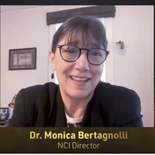 Dr. Monica Bertagnolli, director of the National Cancer Institute, smiling and wearing glasses, addresses the audience via webcam.