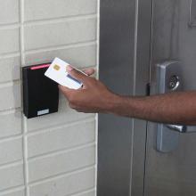A hand scanning a PIV card at a card reader beside a door
