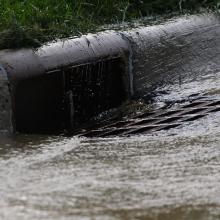 Storm water flows into a storm drain along a road