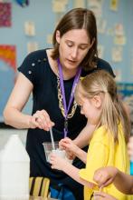 Volunteer stirring liquid in a cup while child looks on