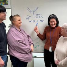 Four people who worked on the study together stand in front of a white board to which the researcher is pointing to a visual of the ADC.