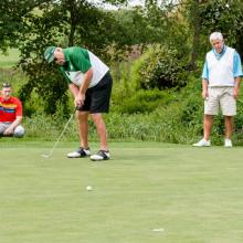 Man putts as two players watch