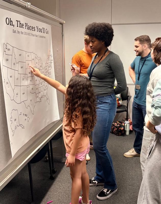 A young visitor discusses where different fellows are moving with one of the postbac fellows who will be departing NCI Frederick. (Image credit: Karolina Wilk)