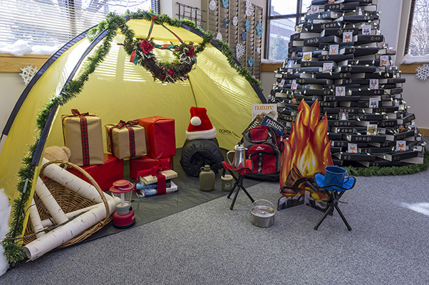 Perhaps the library’s most impressive tableau from the 2019 Holiday Decorating Contest was a miniature camping scene flanked by the famous “book tree.” The tree, made of outdated reference volumes, had occupied a corner of the library’s seating area for years and was seasonally redecorated to boost patrons’ morale. (Photo from the SPGM archive.)