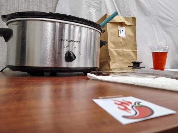 A slow cooker beside a paper bag and a cup filled with spoons
